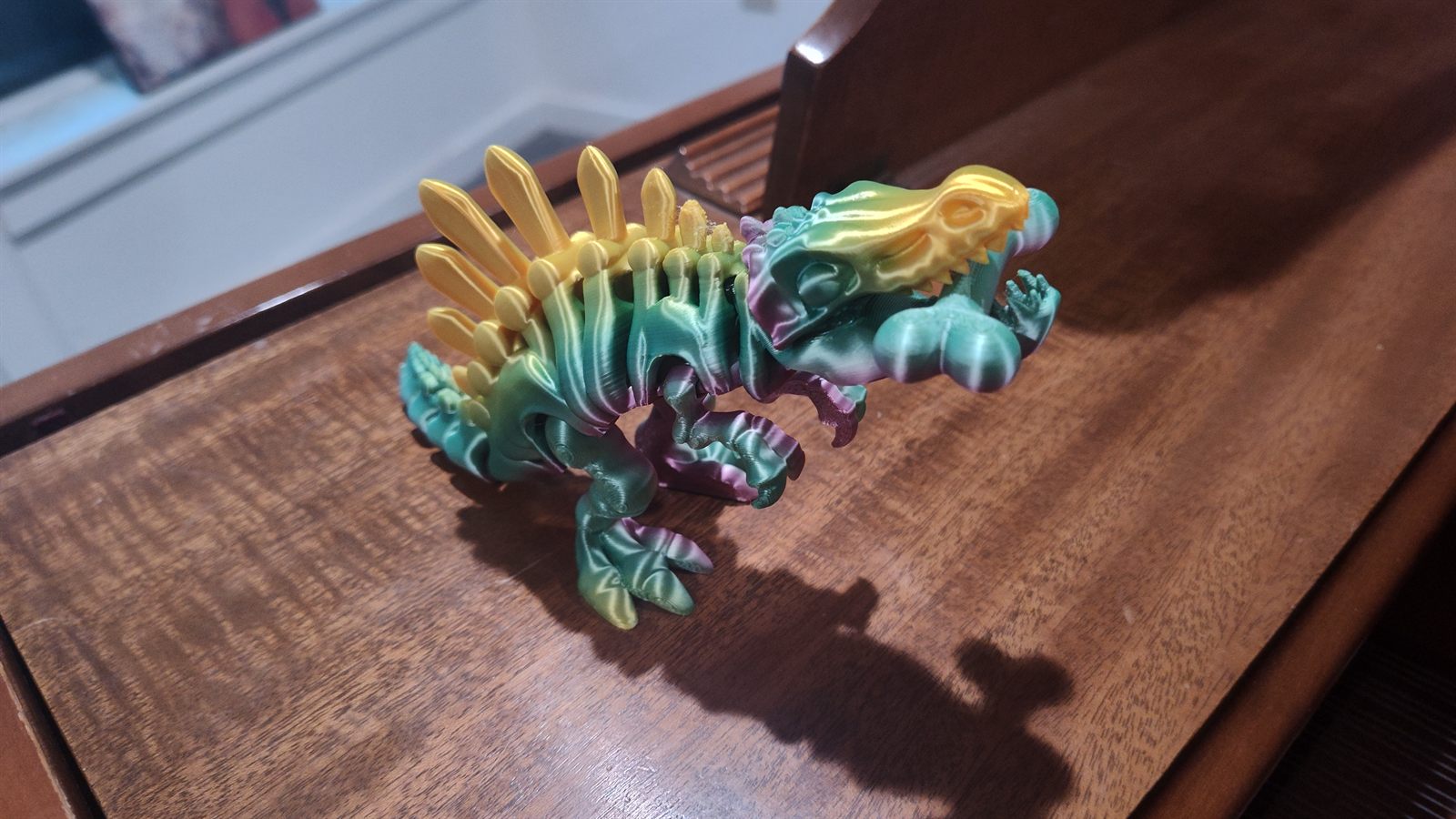 A multi-color articulated Spinosaurus print on a wood surface
