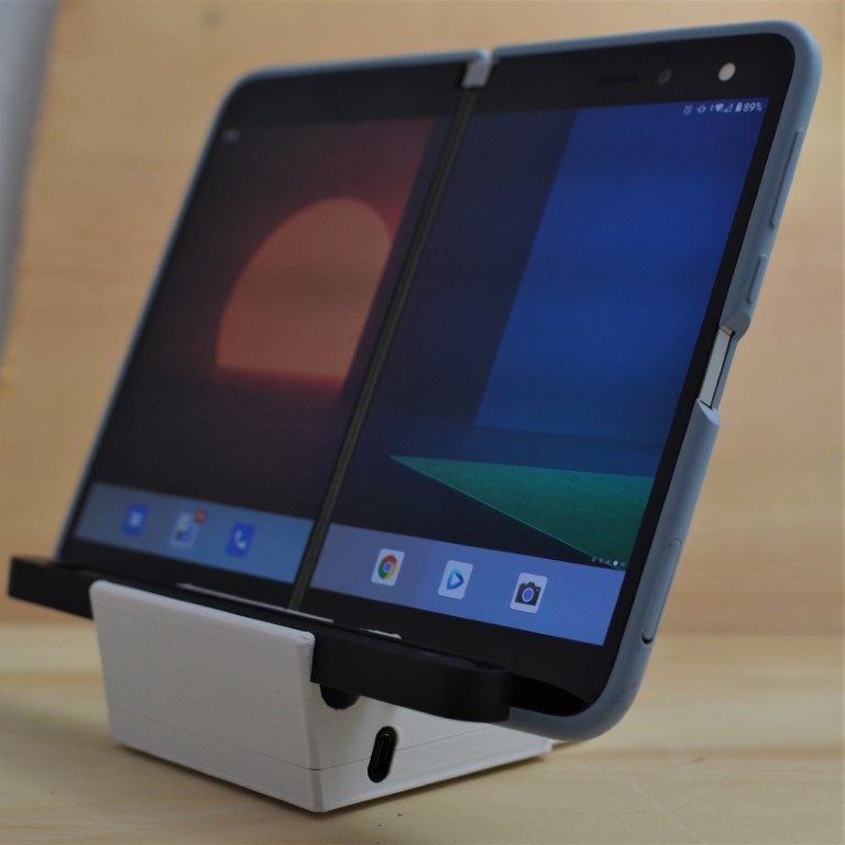 A Surface Duo phone propped up on a white 3D-printed angled dock with a Surface Slim Pen slot
