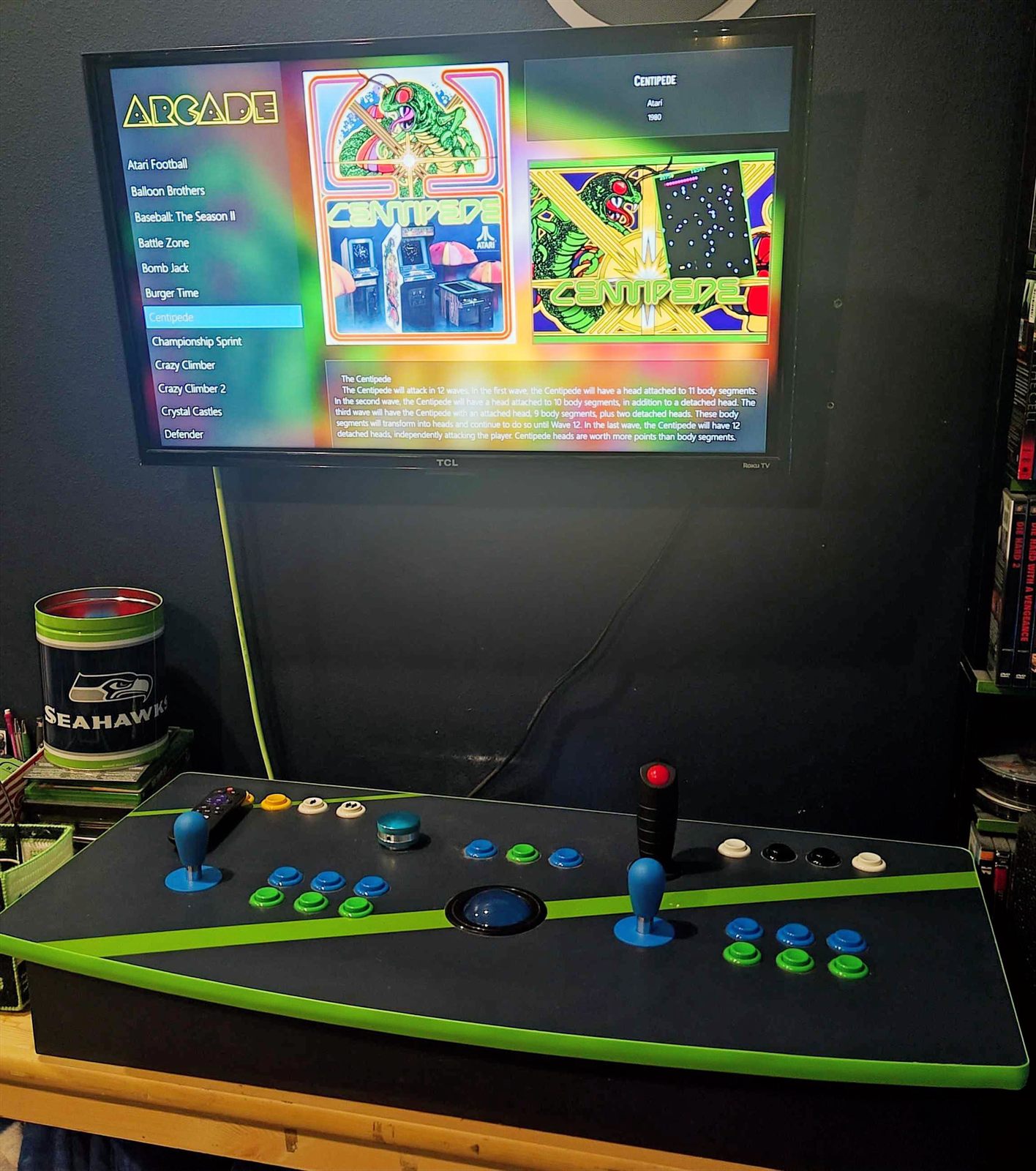 The arcade cabinet on a table beneath a TV running the LaunchBox/BigBox arcade UI on the Centipede game