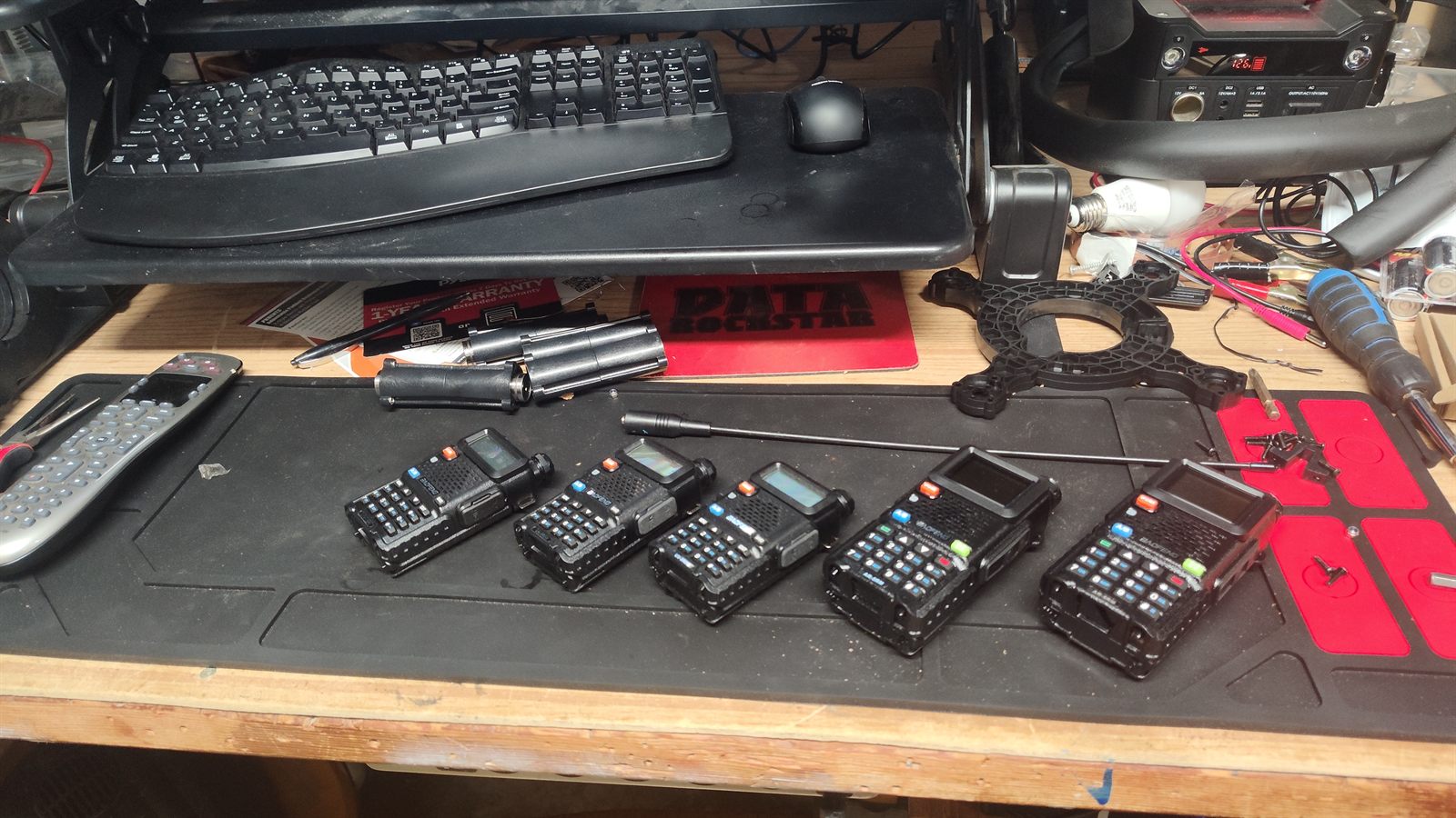 Five Baofeng dual-band handheld transceivers lined up on a workbench mat